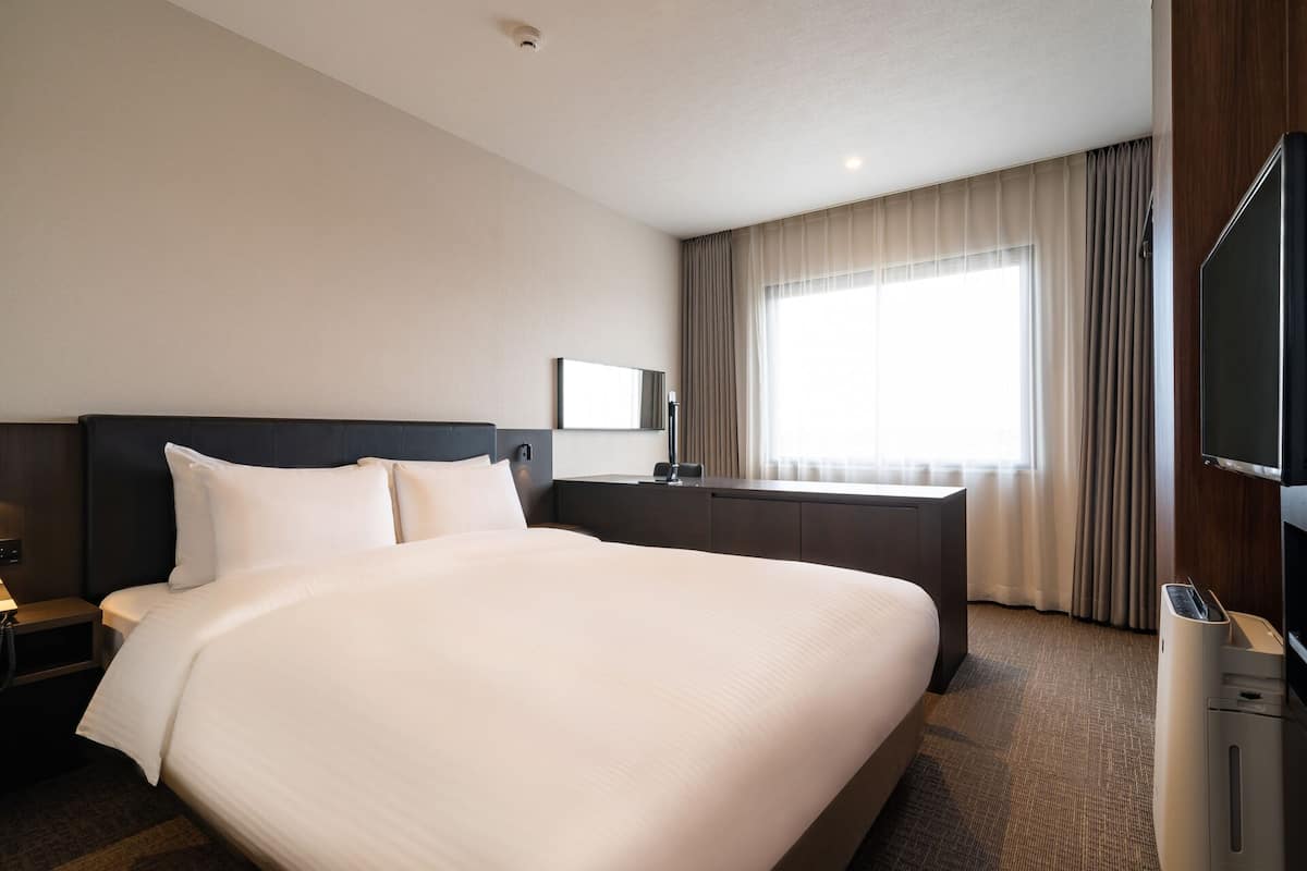 A hotel room with a large bed, a desk, a chair, a television, and a window with curtains.
