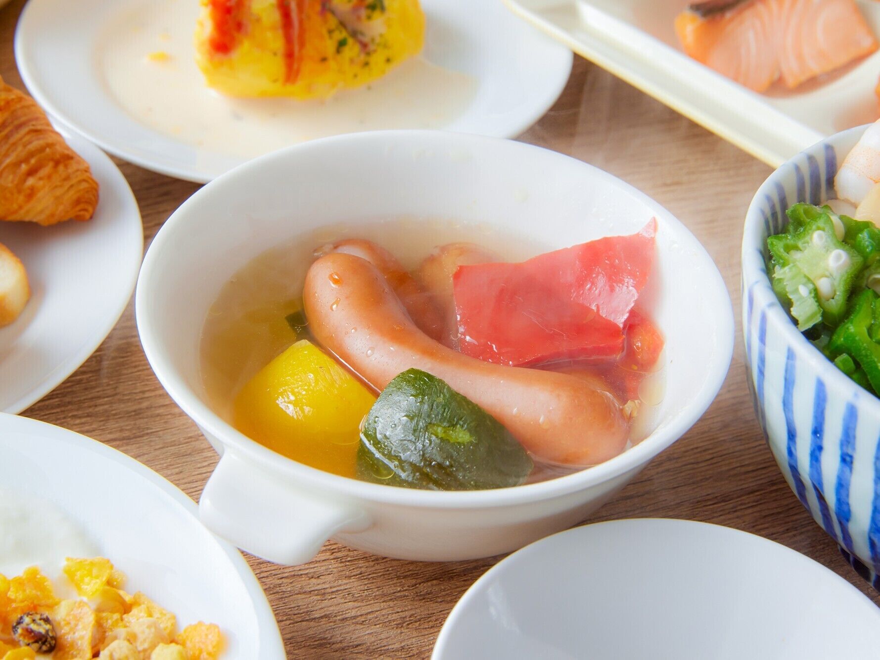 A bowl of soup with various ingredients, surrounded by other dishes on a wooden table.