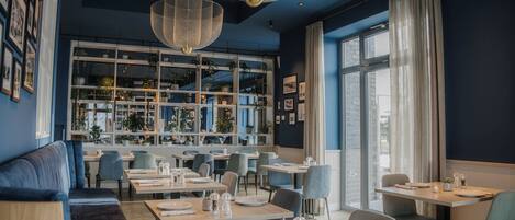 A modern restaurant with a blue interior, large windows, and a variety of seating options including tables and a sofa.