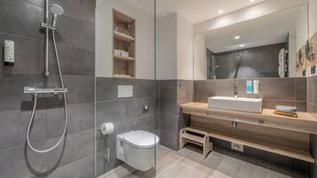 Un baño moderno con ducha envuelta en vidrio, un inodoro blanco, un tocador de madera con espejo y un estante empotrado.