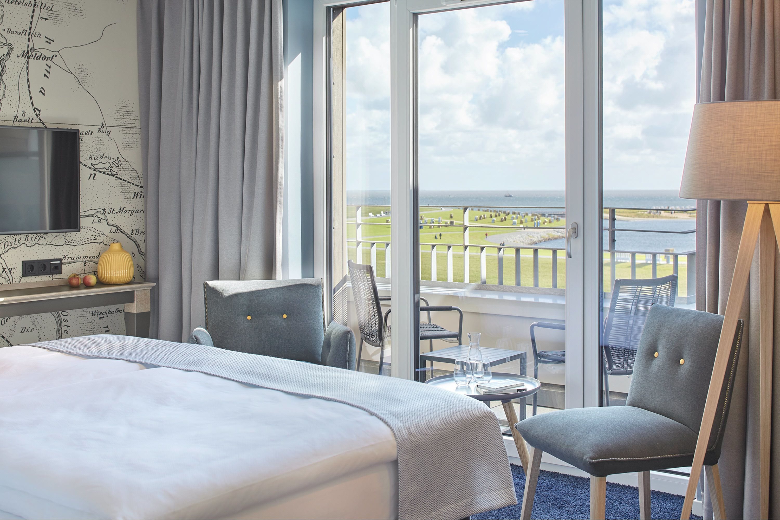 Une chambre d’hôtel avec un lit, un bureau, une chaise, une télévision et un balcon donnant sur la mer.