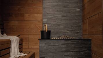 A wooden bench with a white towel, a black bucket with a wooden handle, and a stone wall.