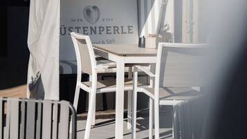 An outdoor seating area with a covered table and chairs, a sign with the name "JÜSTENPERLE Hotel & Spa", and a view of the building in the background.