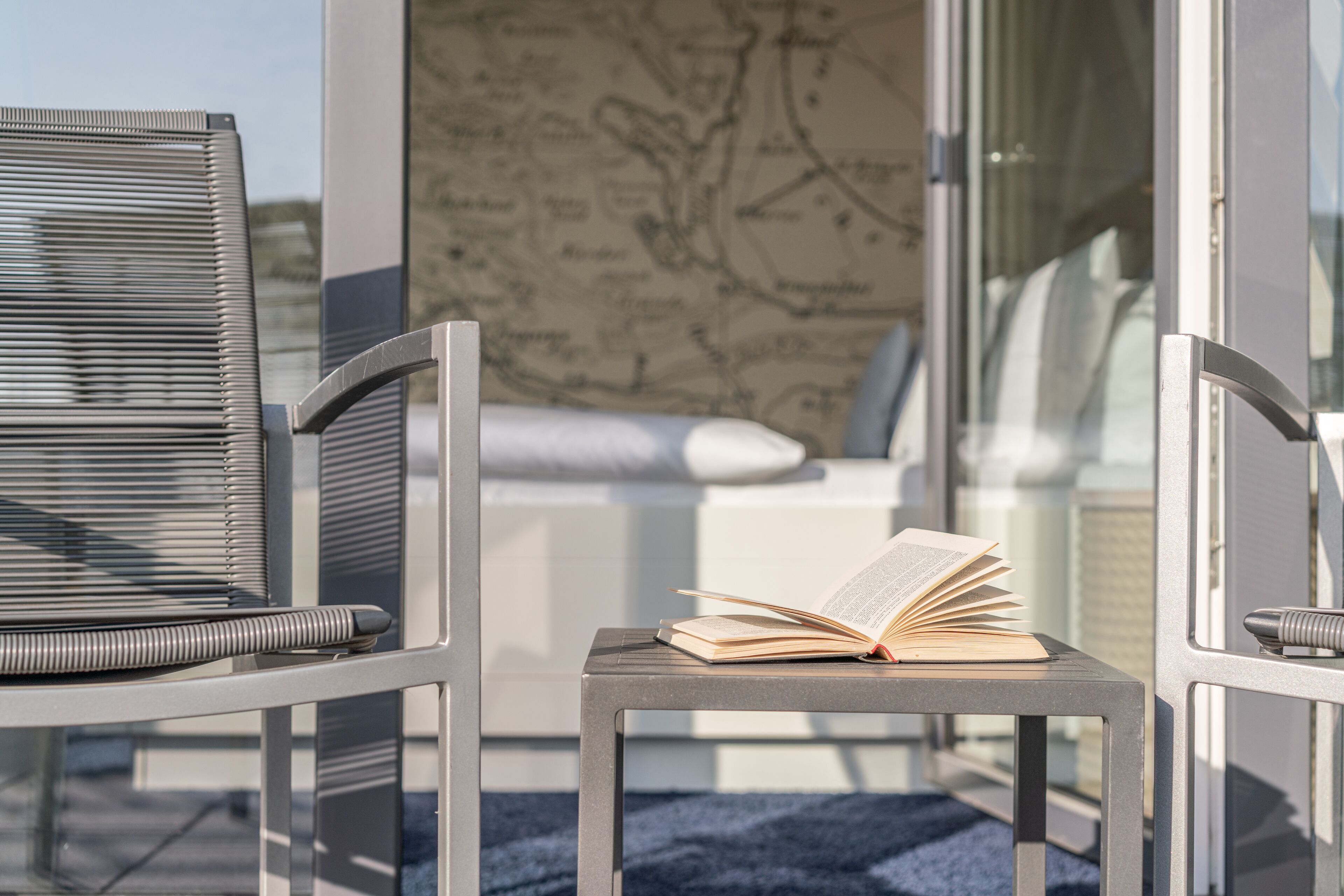 A modern balcony with two metal chairs, a small table, and an open book.