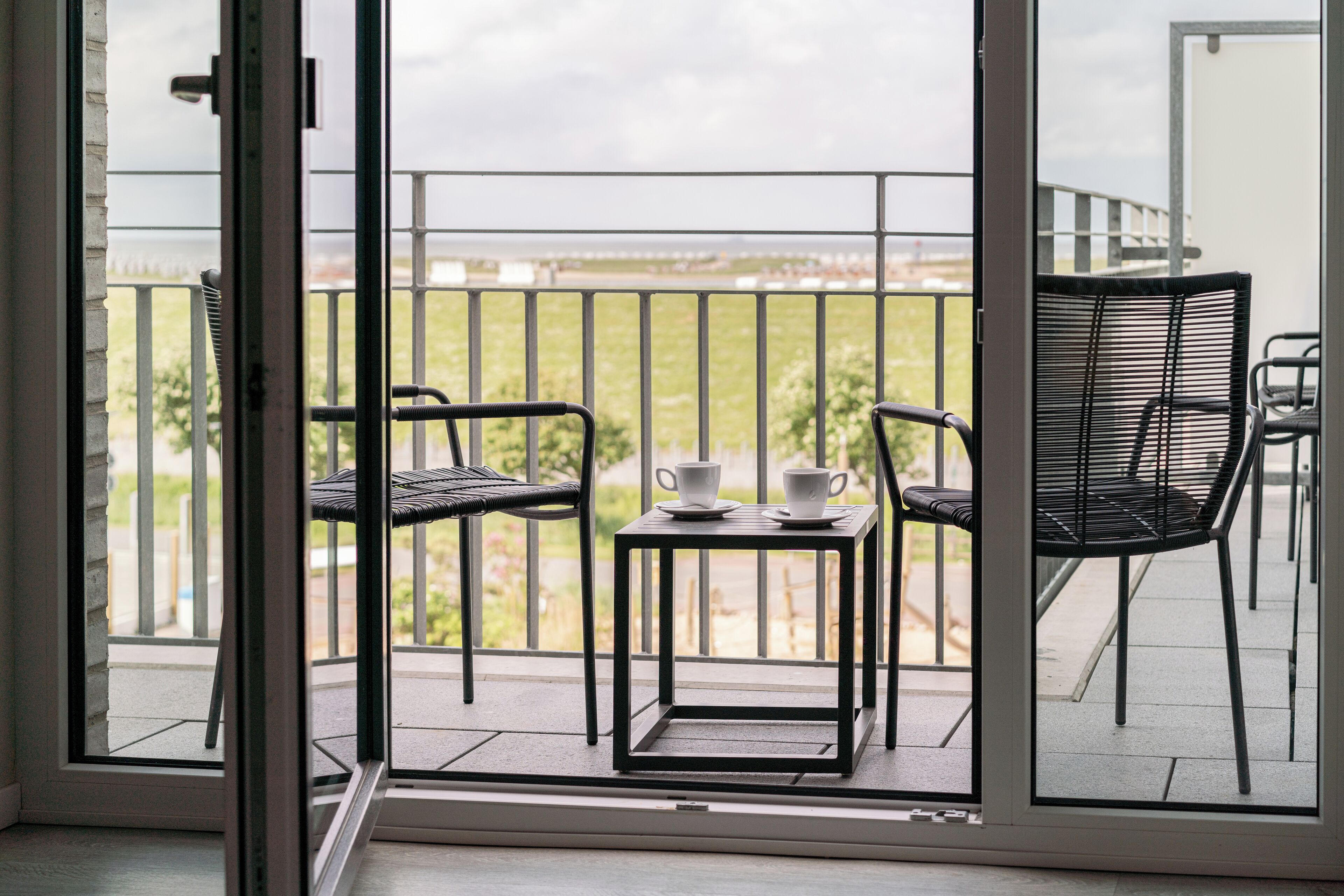 Un balcon avec deux chaises et une petite table, chacune agrémentée d’une tasse.