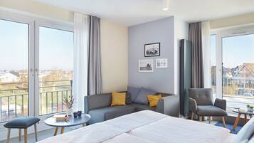 Ein modernes Hotelzimmer mit einem großen Bett, einem Sofa, einem Sessel und einem kleinen Tisch. Große Fenster mit Vorhängen, ein Balkon und Blick auf die Stadt.