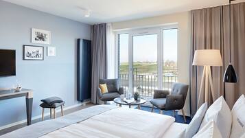 Une chambre d’hôtel avec un grand lit, deux fauteuils, une petite table, un bureau, une télévision et un balcon avec vue.