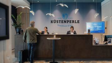 Un mostrador de recepción en KÜSTENPERLE Strandhotel & Spa con un diseño moderno, una pantalla digital que muestra información y un suelo con estampado.