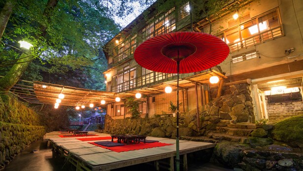 Un espace extérieur aménagé pour les repas, avec des tables et des chaises, un parasol rouge et un mur en pierre.