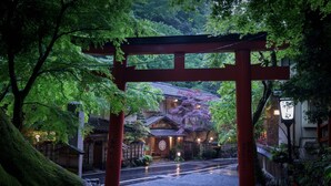 Un portail torii japonais traditionnel, situé dans un jardin luxuriant, avec un bâtiment en arrière-plan.