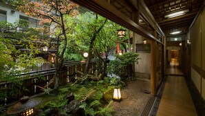 Un jardin japonais traditionnel avec une allée en bois, des lanternes en pierre et une végétation luxuriante.