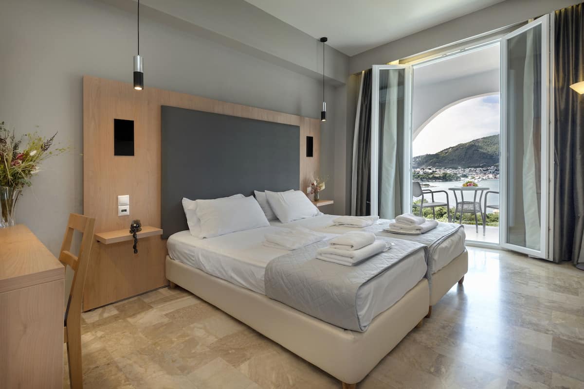 Ein modernes Hotelzimmer mit einem großen Bett, einem Holzkopfschild, einem kleinen Schreibtisch und einem Balkon mit Blick auf die Stadt.