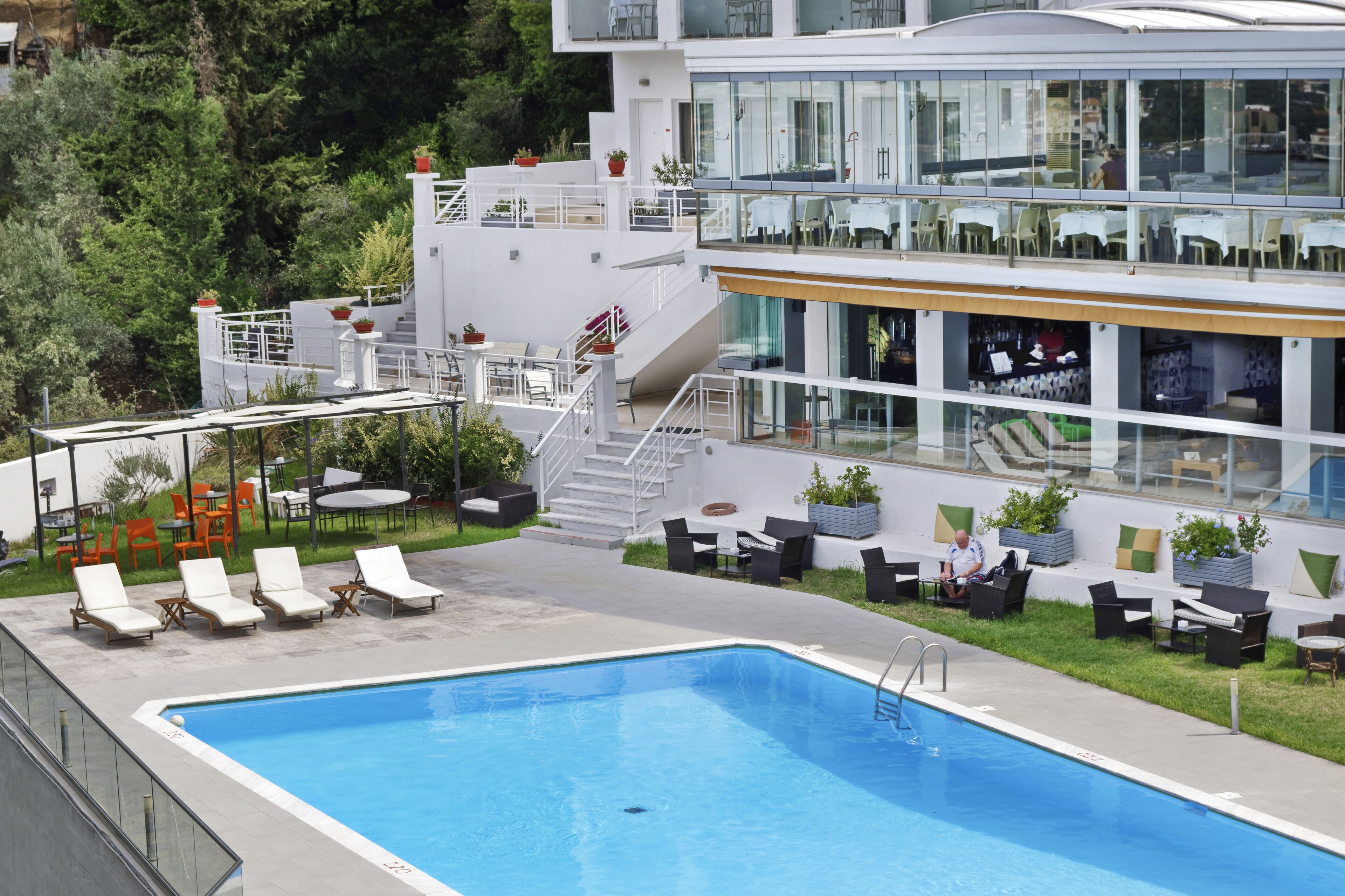 A modern hotel with a swimming pool, outdoor seating, and a restaurant with glass walls.
