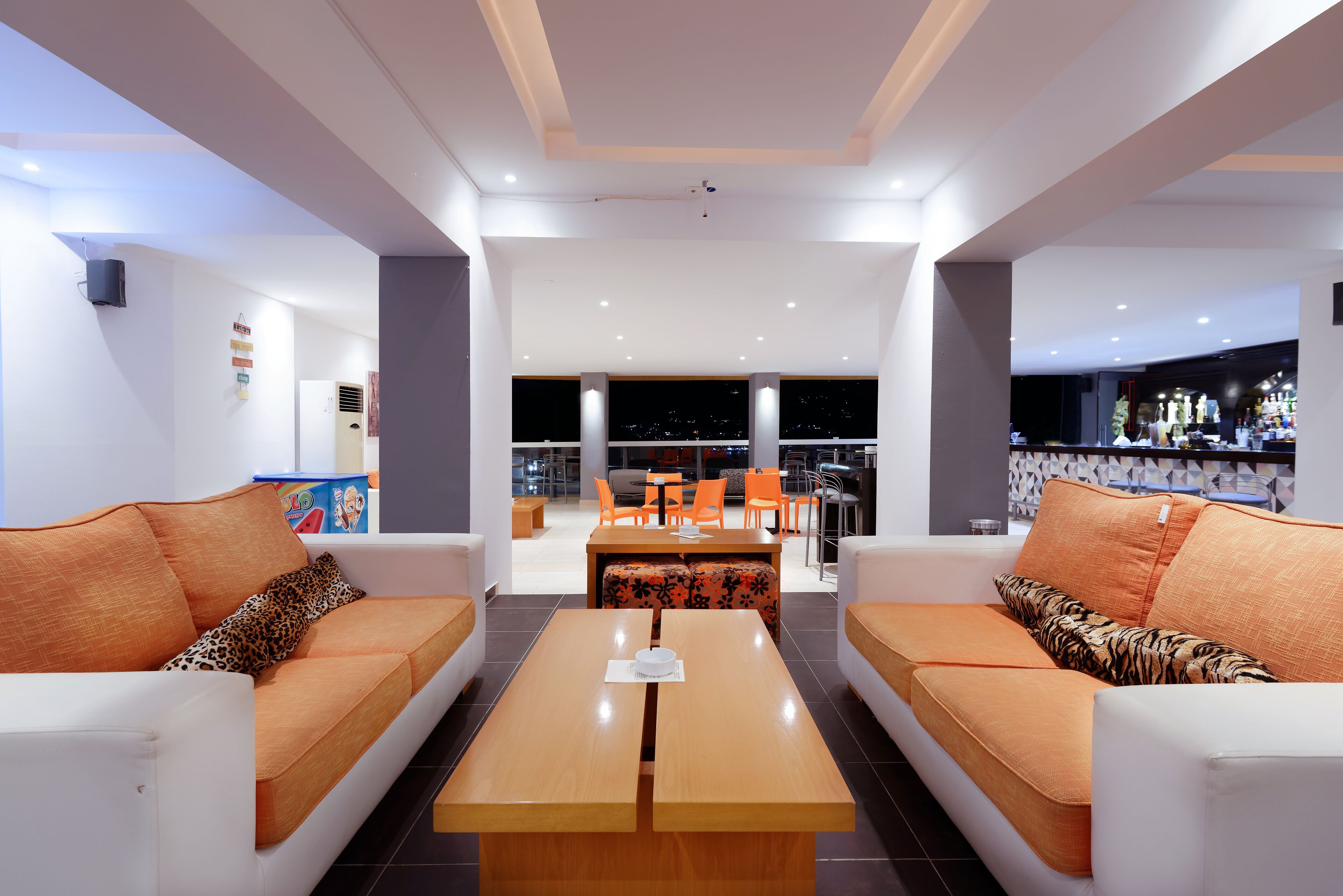Una sala de estar moderna con una mesa de centro, dos sofás con cojines estampados, un comedor con sillas y una barra de bar al fondo.