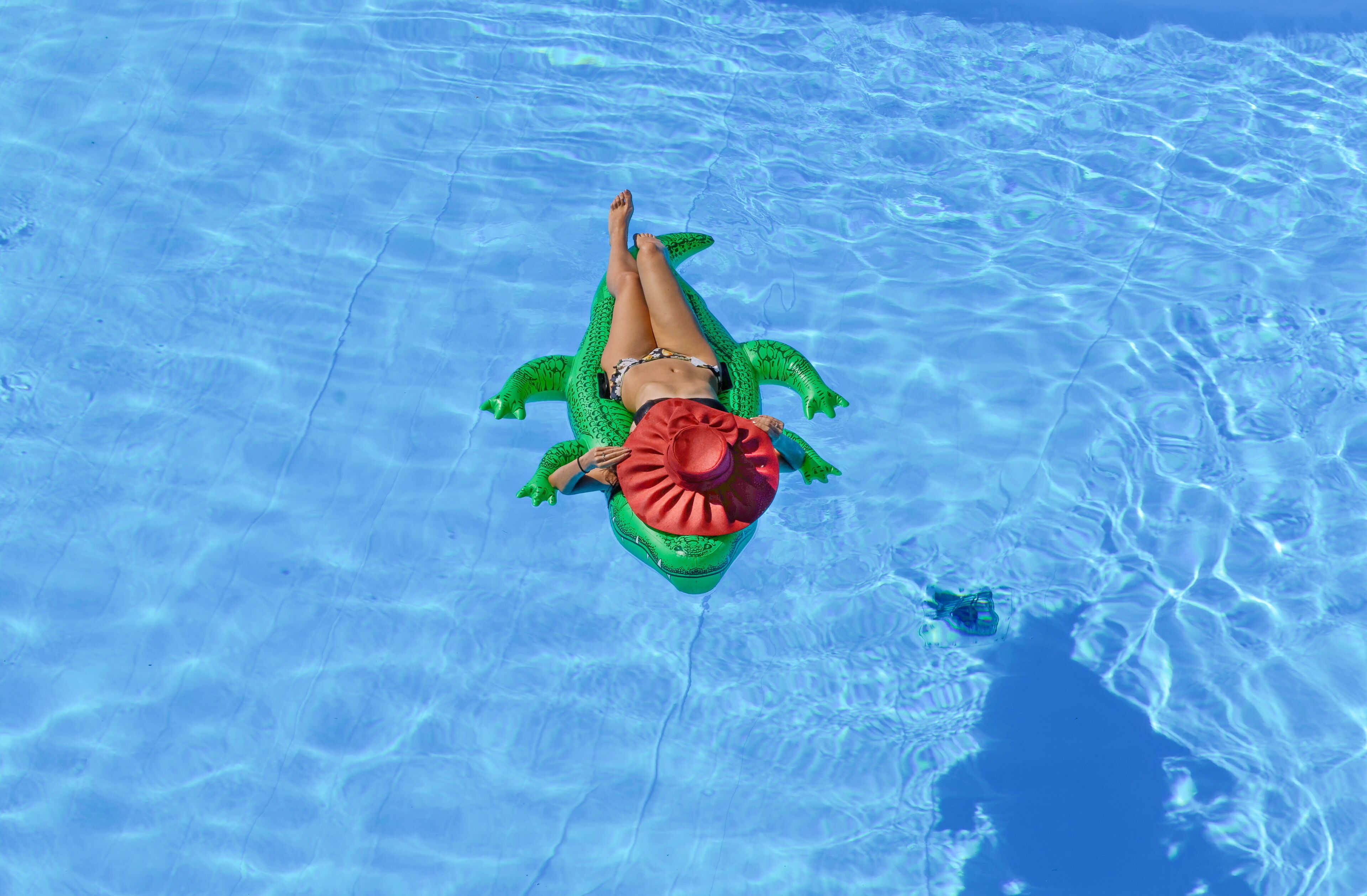 A person floating on a green inflatable pool float in clear blue water.