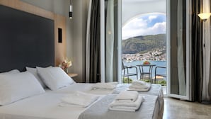 Ein Hotelzimmer mit einem großen Bett, einem Balkon mit Tisch und Stühlen und Blick auf eine Küstenstadt.