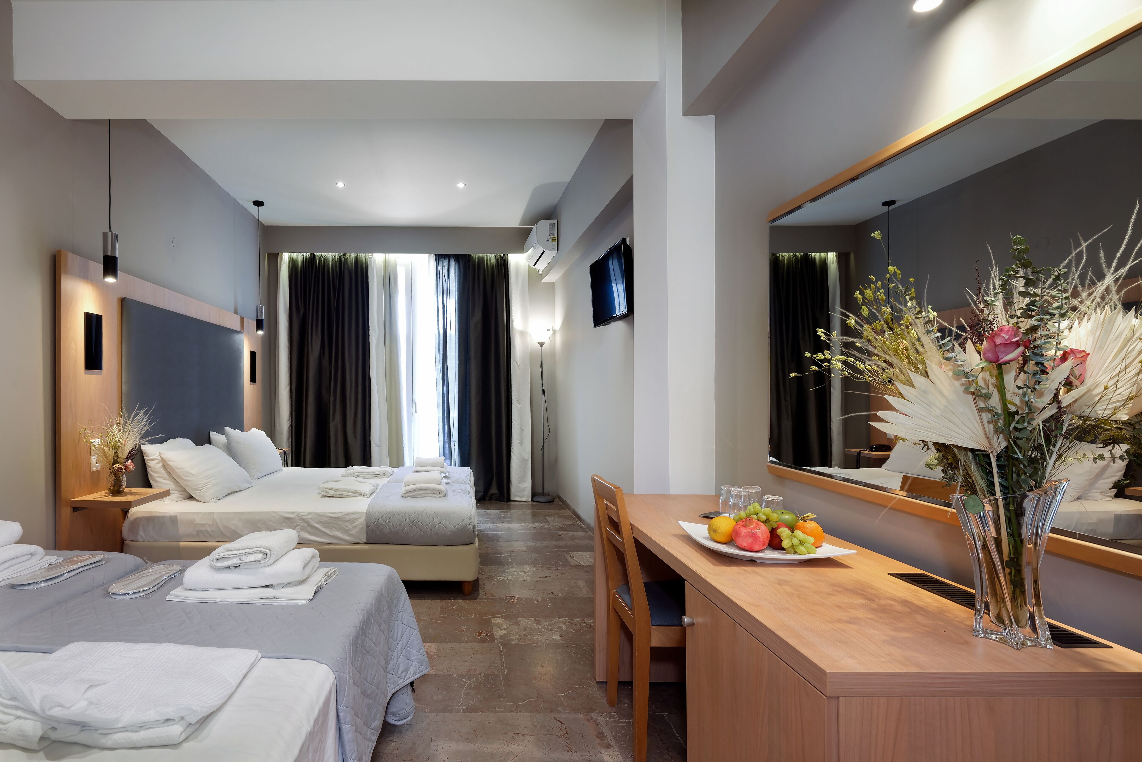 Een hotelkamer met twee bedden, een bureau met een bloevas en een grote spiegel.