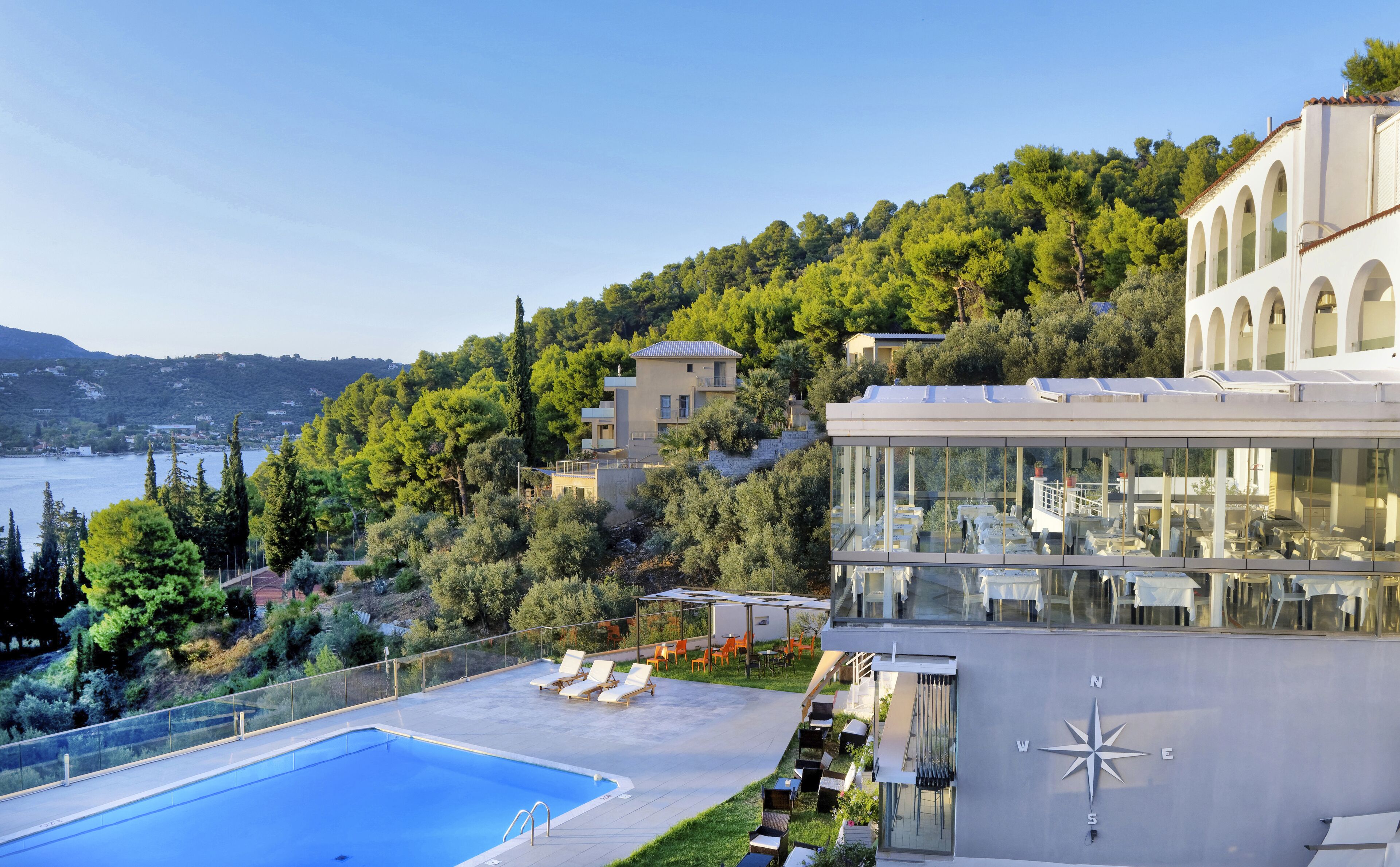 A modern building with a rooftop pool, surrounded by lush greenery and overlooking a body of water.