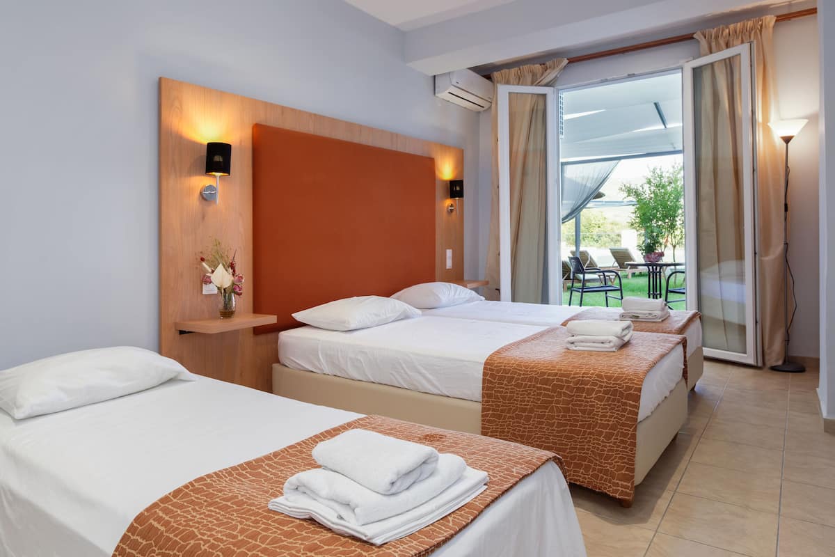 Ein Hotelzimmer mit zwei Betten, einem Holzkopfende, einem kleinen Tisch mit einer Vase und Blick ins Freie.