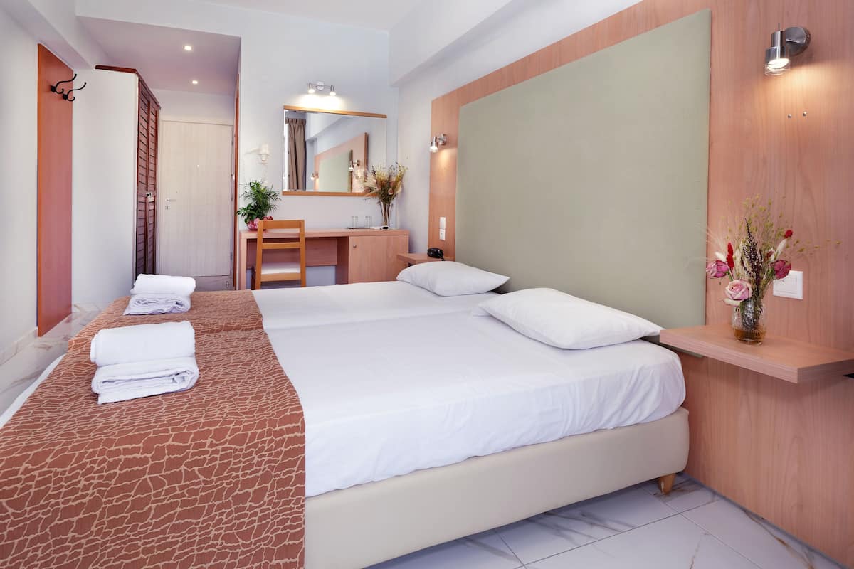 Ein Hotelzimmer mit einem großen Bett, einem Schreibtisch, einem Spiegel und einem an der Wand befestigten Regal mit Blumen.