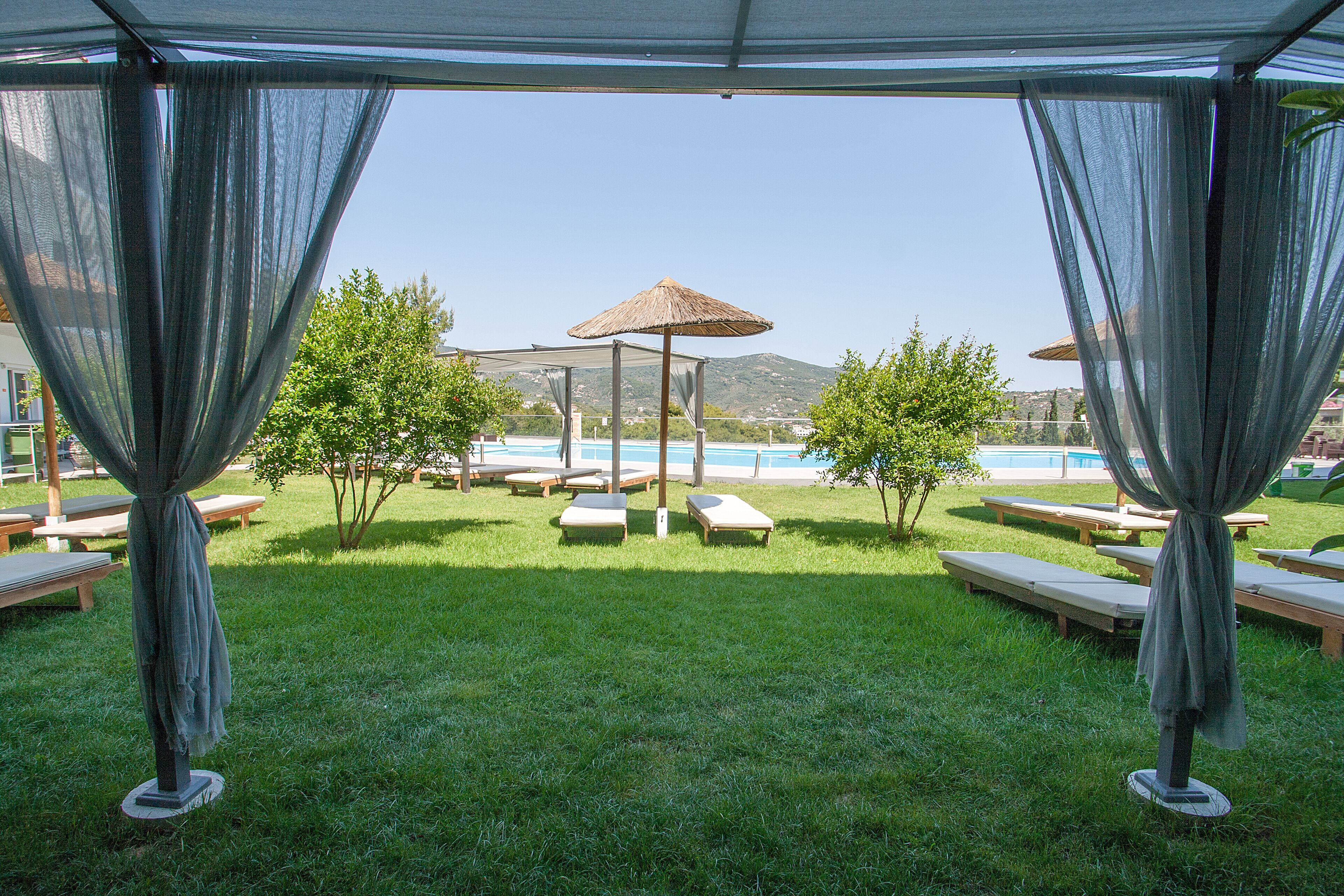 A poolside area with lounge chairs and umbrellas, a clear view of the pool, and a mountainous backdrop.