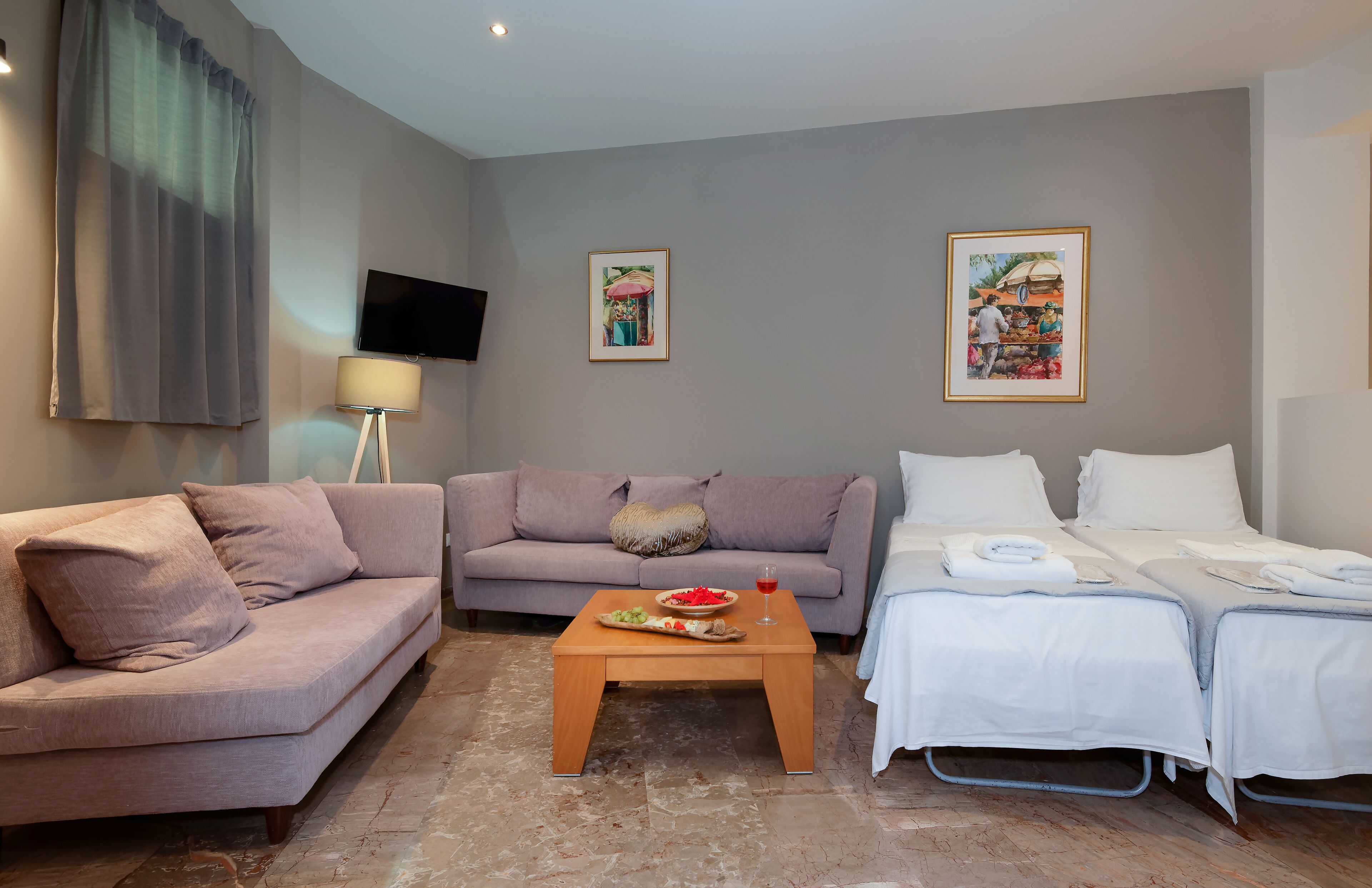 Ein modernes Hotelzimmer mit einer Couch, einem Bett, einem kleinen Holztisch mit einer Obstplatte und zwei gerahmten Kunstwerken an den Wänden.