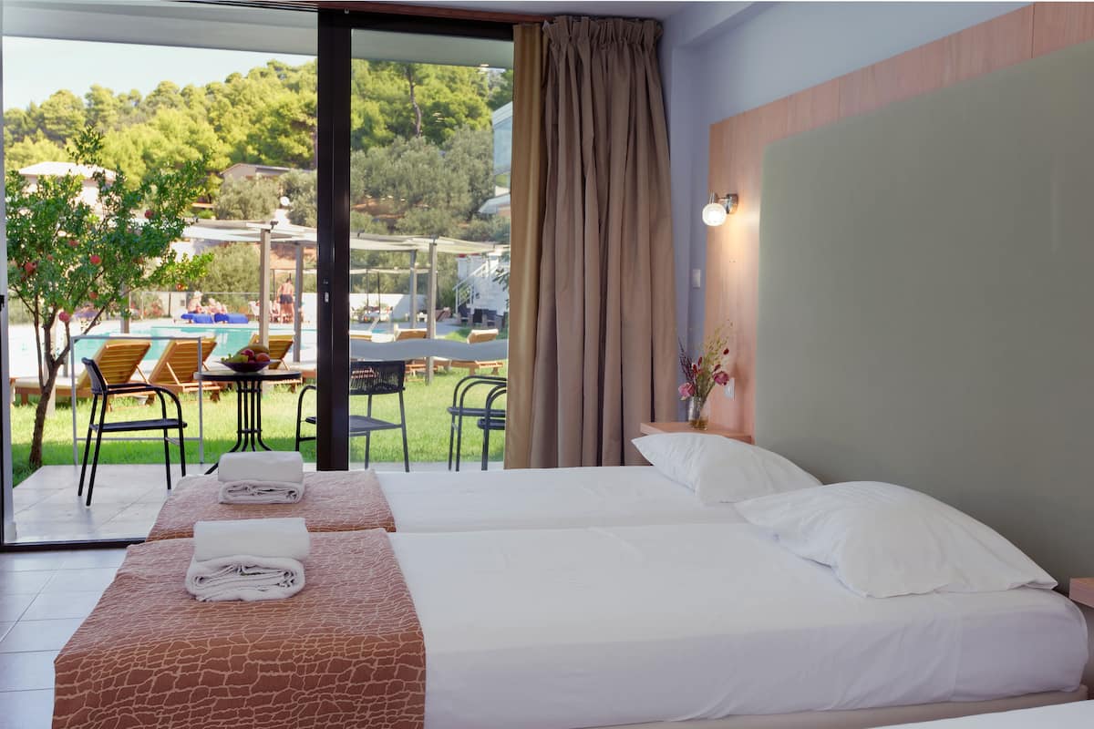 Ein Hotelzimmer mit zwei Betten, Blick auf den Außenpool und einem Esstisch mit Stühlen.