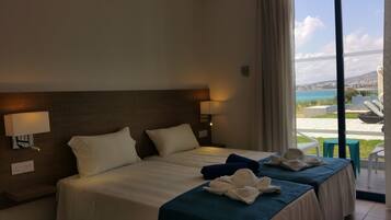 Habitación de hotel con cama, dos almohadas, lámpara de noche, ventana con vista al mar y una toalla sobre la cama.