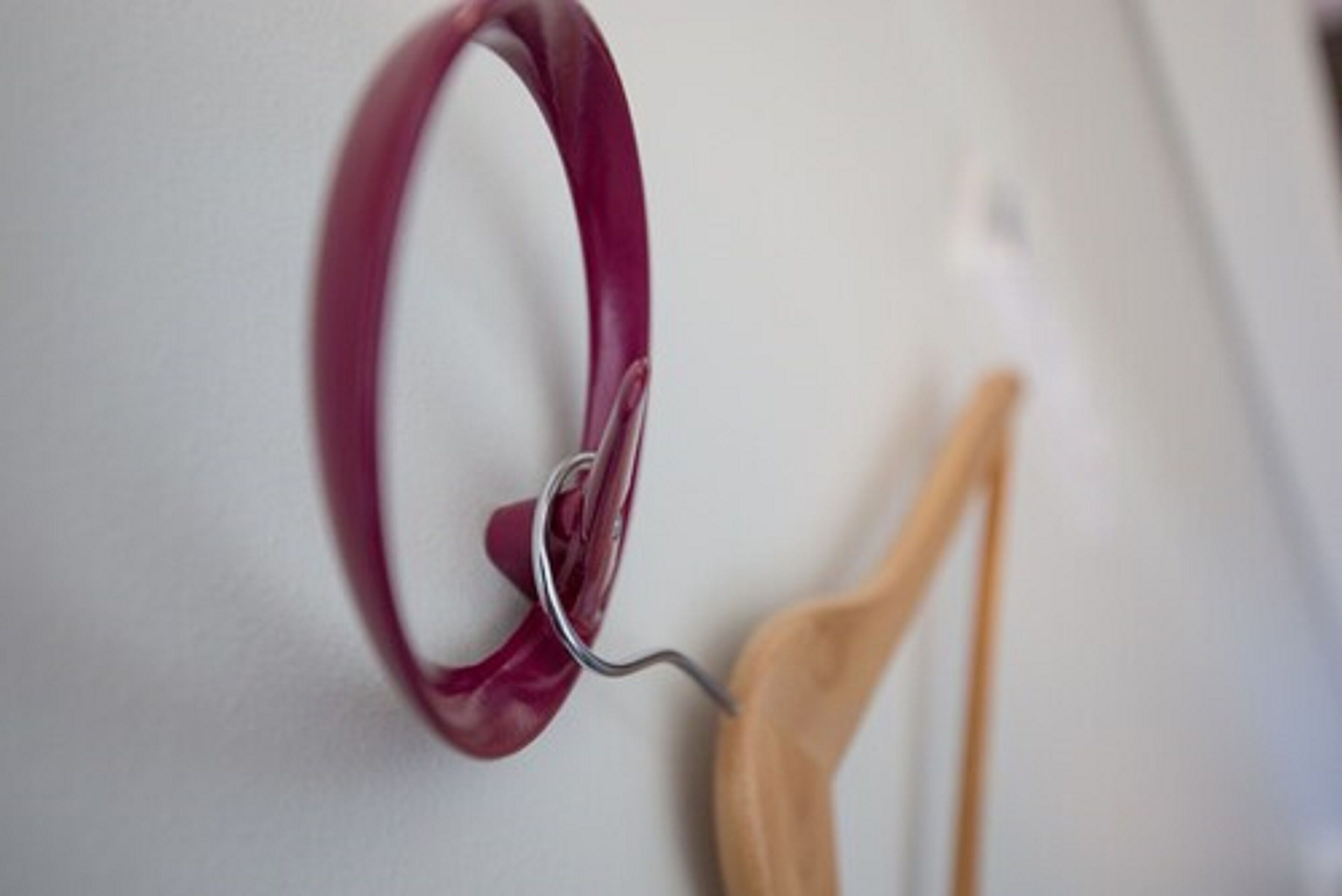 A close-up of a red circular object, possibly a handle or part of a piece of furniture, attached to a wall with a metal hook.
