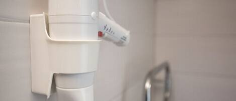 A white hair dryer mounted on a wall next to a metallic faucet.