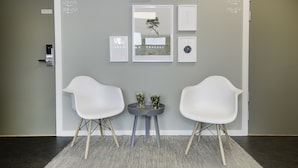 A reception area with a reception desk, two white chairs, and framed artwork on the wall. - Hotell Eken (Kållered)