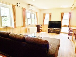 A living room with a sofa, a flat-screen TV, a wooden cabinet, and a dining table with chairs. - Resort House Niseko First (Niseko)