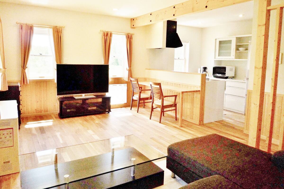 A compact living space with a flat-screen TV, a sofa, a dining area, and a kitchenette.