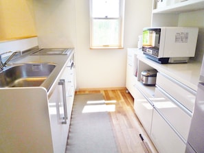 A small kitchen with a sink, stove, microwave, and cabinets. - Resort House Niseko First (Niseko)