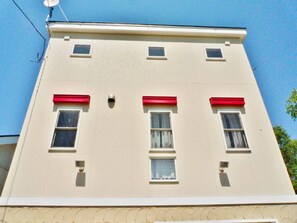 Un edificio con fachada plana, varios ventanales y aleros rojos.