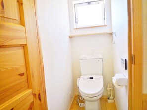 Un baño pequeño y limpio con inodoro blanco, puerta de madera y ventana sobre el inodoro.