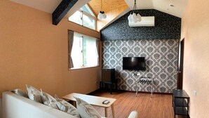 A modern living room with a white sofa, a small table, and a TV mounted on a patterned wall. - BlackJazz Inn (Puli)