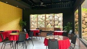 A restaurant with round tables and chairs, red tablecloths, a brick wall, and a large window with a view of rocks and greenery. - BlackJazz Inn (Puli)