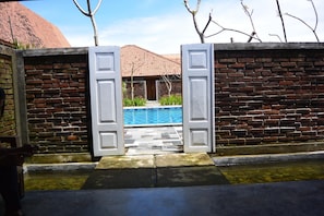 A brick wall with a pool visible through an open gate.