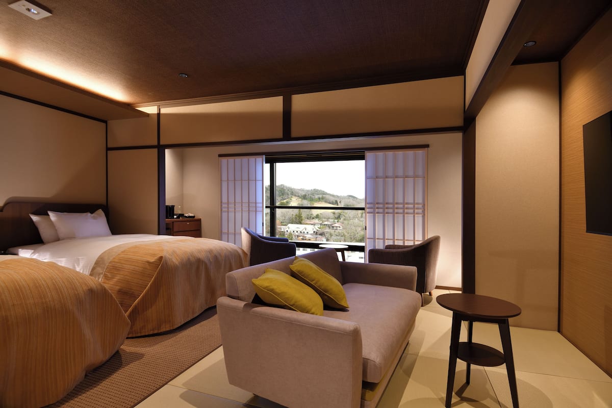 A hotel room with two beds, a sofa, a small table, and a view of the outdoors.