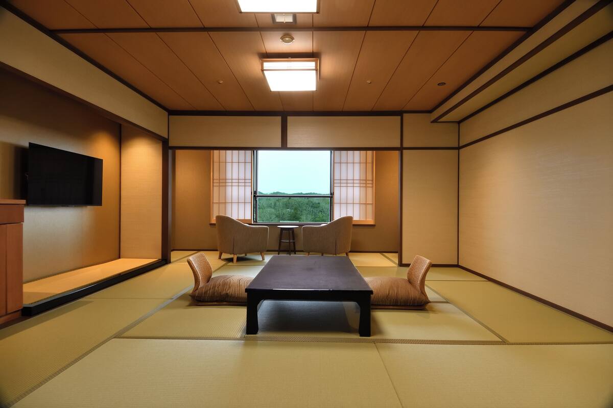 A traditional tatami room with a low table, two cushions, and a television on the wall.