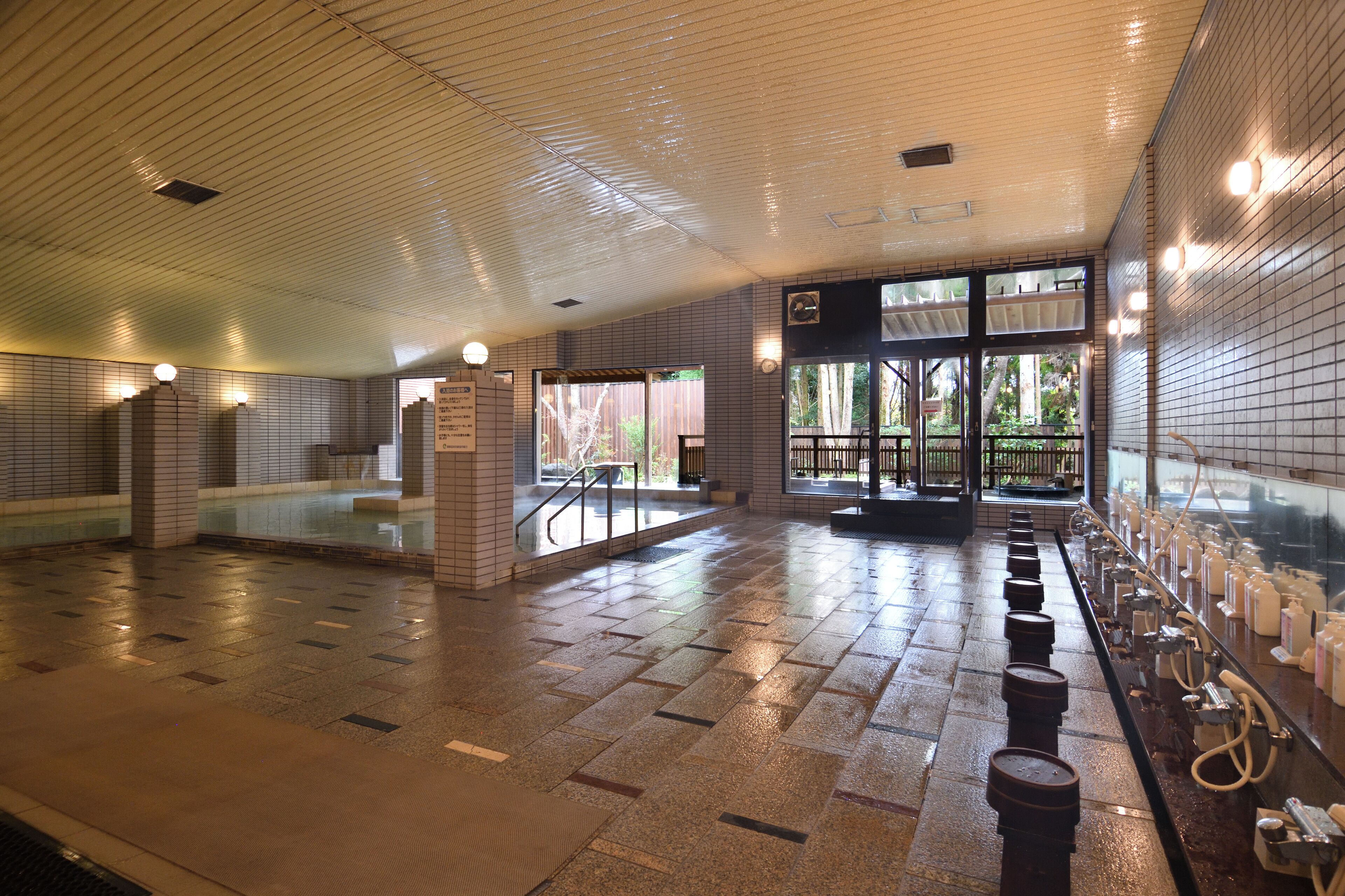 A spacious indoor area with tiled floors, a row of sinks, and a glass door leading outside.