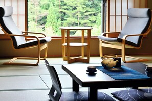 A room with two lounge chairs, a small table, and a view of a forest through large windows. - Yunogo Onsen HOTEL YUNOMORI (Mimasaka)