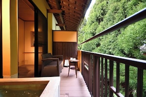 A balcony with a wooden floor, a hot tub, wicker furniture, and a view of dense green trees. - Yunogo Onsen HOTEL YUNOMORI (Mimasaka)
