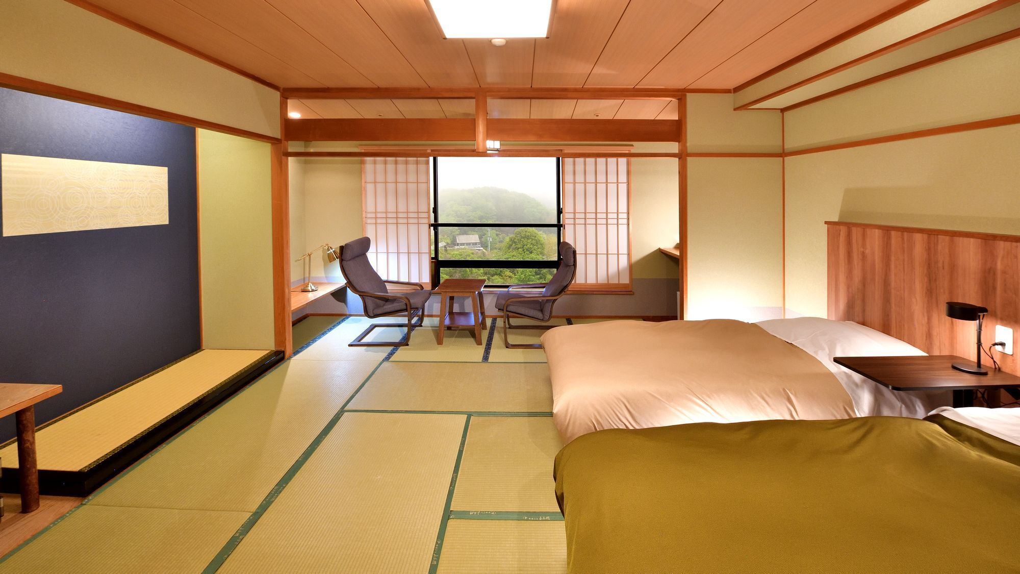 A traditional Japanese-style hotel room with tatami flooring, a bed, a desk, and a view of the outdoors.
