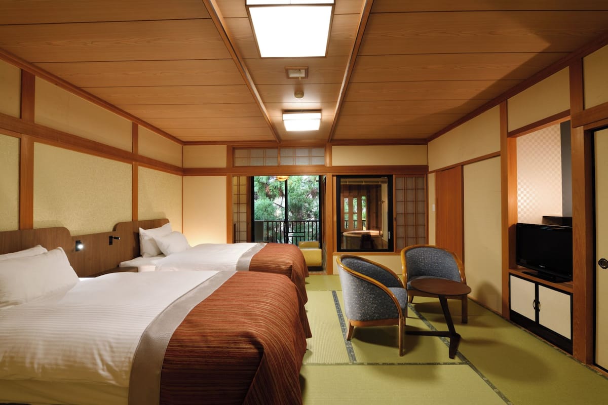 A traditional Japanese-style hotel room with two beds, a television, and a view of the outdoors.