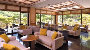 A spacious indoor area with multiple seating arrangements, large windows offering views of a garden, and a ceiling with a grid-like pattern. - Yunogo Onsen HOTEL YUNOMORI (Mimasaka)