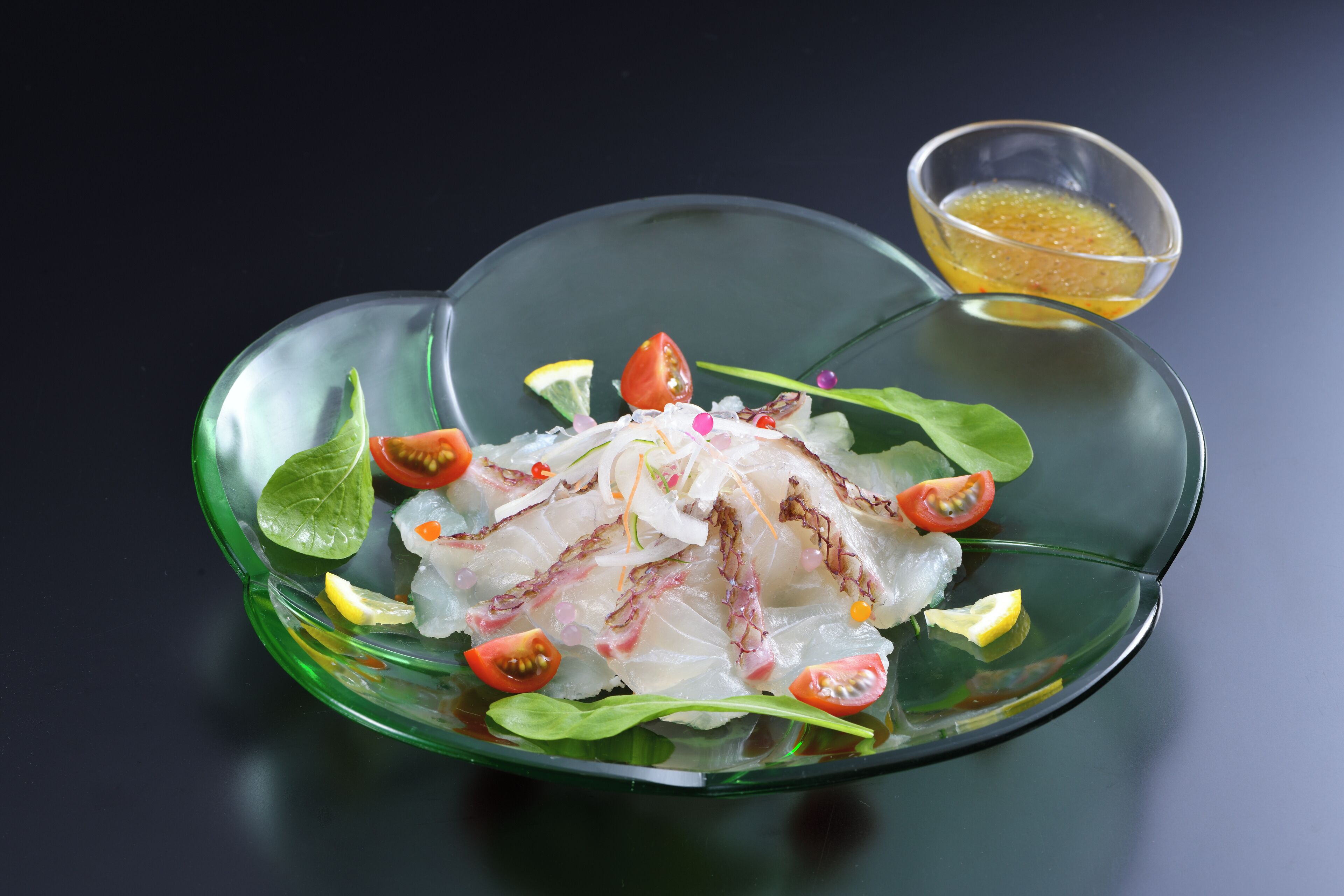 A glass plate with a seafood dish, garnished with lemon and chili, and a small bowl of sauce.