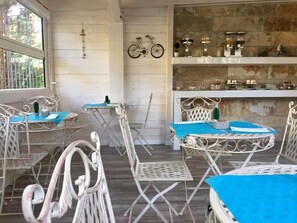 Un coin repas rustique avec des tables et des chaises en métal, un mur en pierre et un vélo accroché au mur.