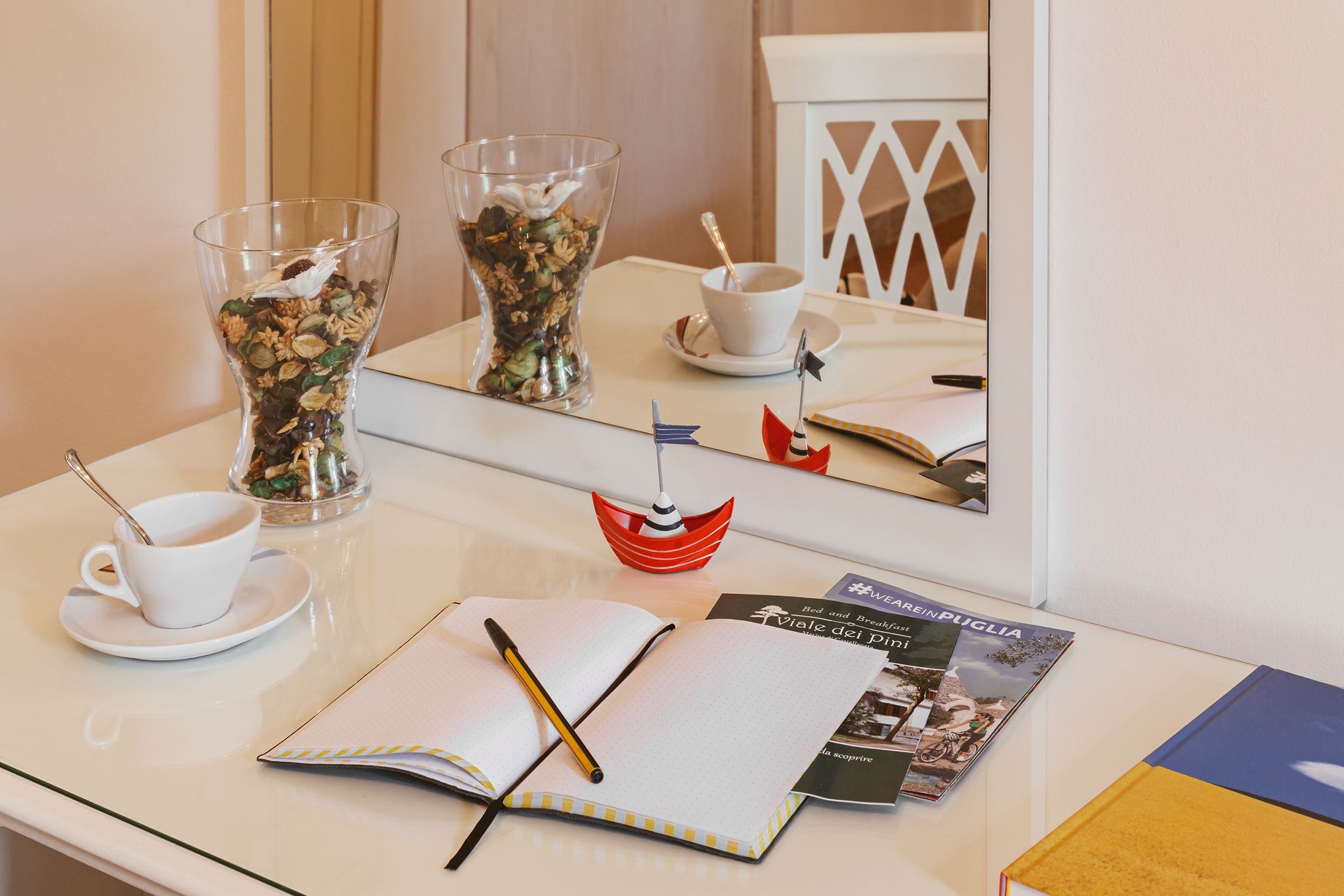 A neatly arranged table with a cup of coffee, a glass of cereal, a notebook, a pen, and a small decorative boat.